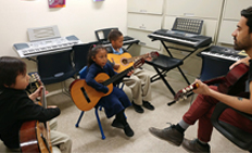 Students learning to play the guitar with the help of an instructor