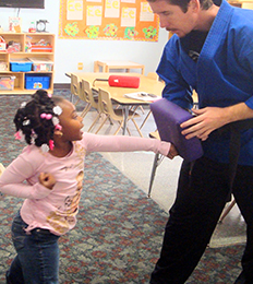 Female student punching a pillow during a karate activity with the help of an instructor